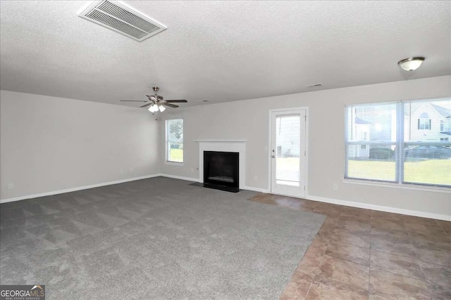 unfurnished living room with ceiling fan, dark tile patterned floors, a textured ceiling, and a wealth of natural light