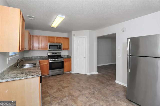 kitchen featuring sink, stone countertops, a textured ceiling, and appliances with stainless steel finishes