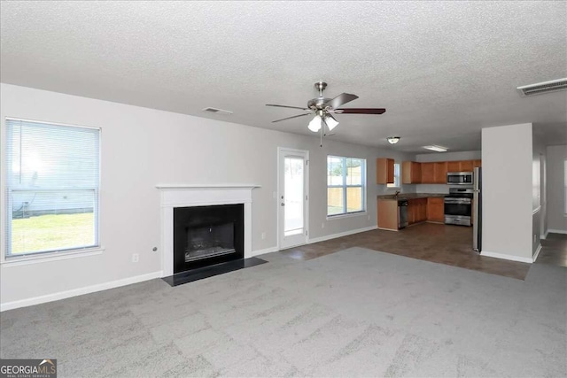 unfurnished living room with ceiling fan, sink, carpet floors, and a textured ceiling