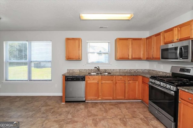 kitchen featuring appliances with stainless steel finishes, plenty of natural light, dark stone countertops, and sink