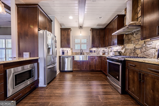 kitchen featuring decorative light fixtures, stainless steel appliances, light stone counters, and wall chimney range hood