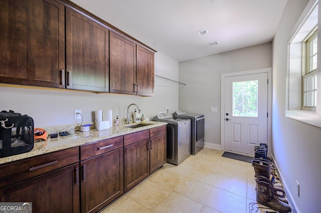 clothes washing area with washing machine and dryer, sink, light tile patterned flooring, and cabinets