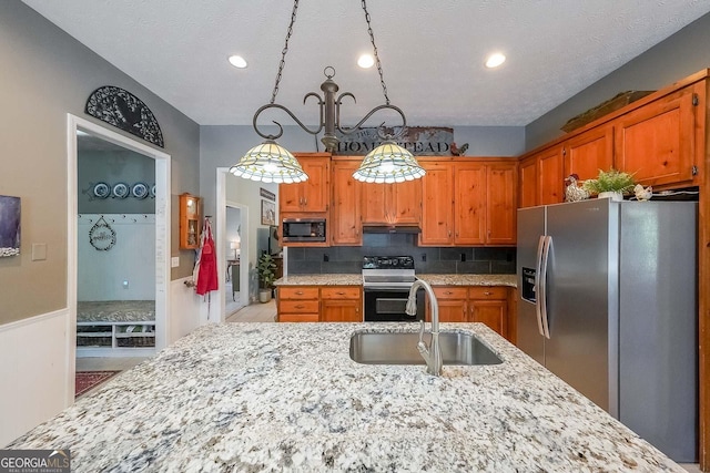 kitchen with sink, light stone counters, a textured ceiling, decorative backsplash, and appliances with stainless steel finishes