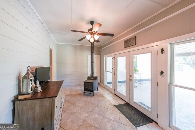 doorway to outside with a wood stove, french doors, crown molding, ceiling fan, and light tile patterned floors