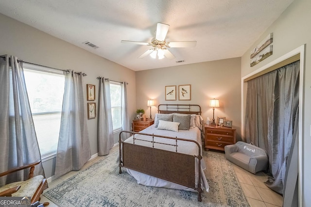 bedroom featuring ceiling fan, light tile patterned floors, a textured ceiling, and a closet