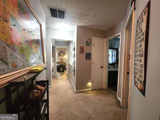 corridor with light carpet, sink, and a textured ceiling