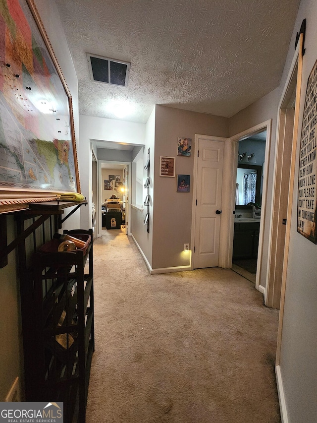 hall featuring light colored carpet and a textured ceiling