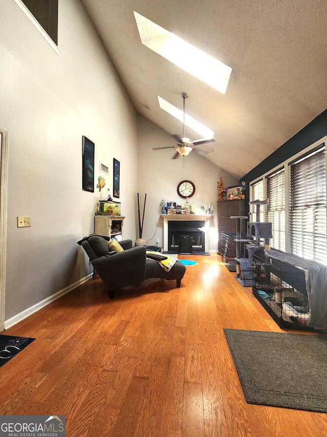 living room with a skylight, high vaulted ceiling, a textured ceiling, ceiling fan, and hardwood / wood-style floors