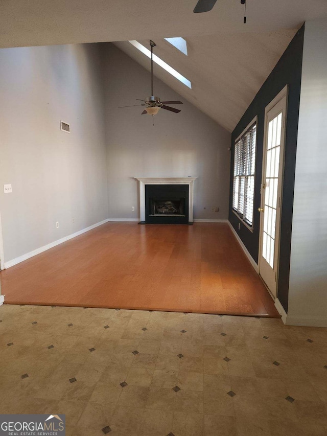 unfurnished living room featuring high vaulted ceiling, ceiling fan, and a skylight