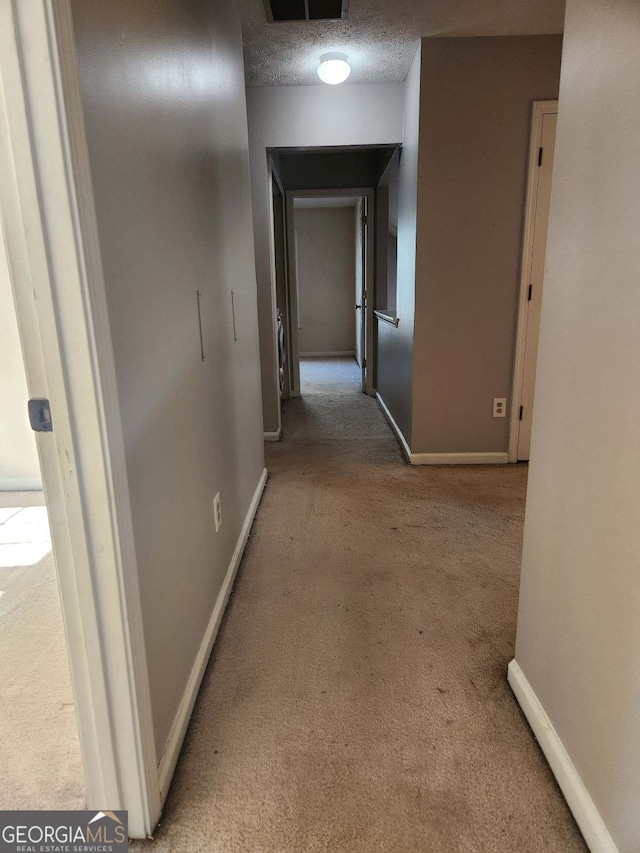 corridor with light colored carpet and a textured ceiling