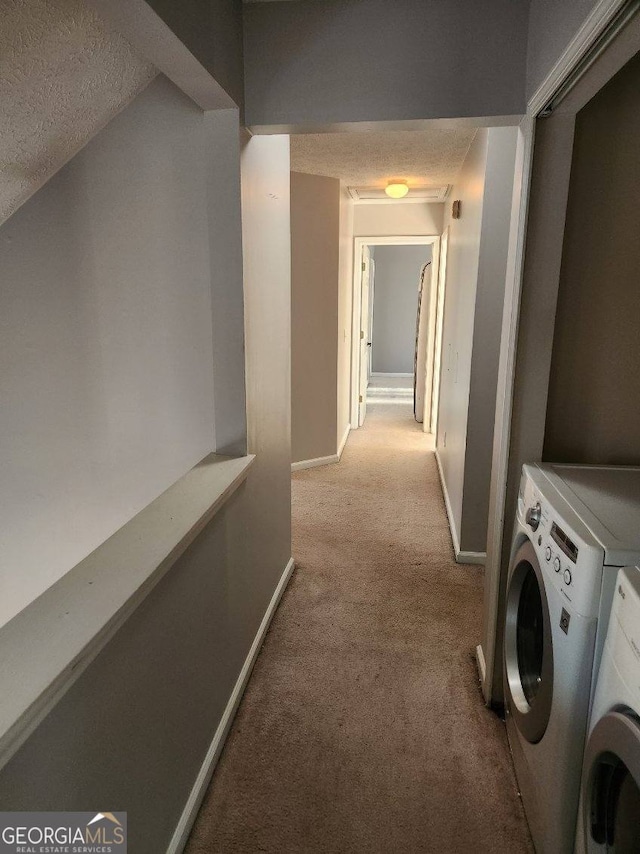 hallway with washer and clothes dryer, light colored carpet, and a textured ceiling