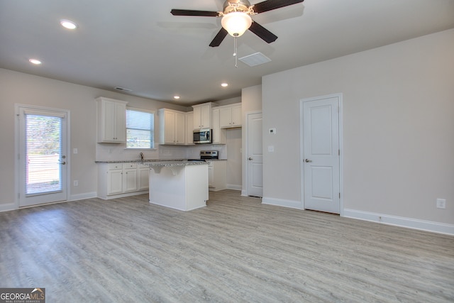 kitchen with light stone counters, light hardwood / wood-style floors, a center island, white cabinets, and ceiling fan