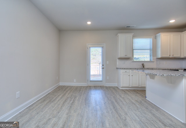 kitchen with light stone counters, light hardwood / wood-style floors, white cabinetry, a kitchen bar, and decorative backsplash