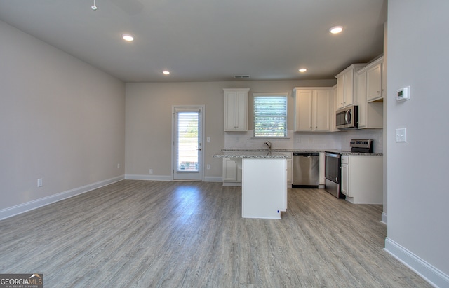 kitchen featuring white cabinetry, a kitchen island, light stone countertops, stainless steel appliances, and light hardwood / wood-style flooring