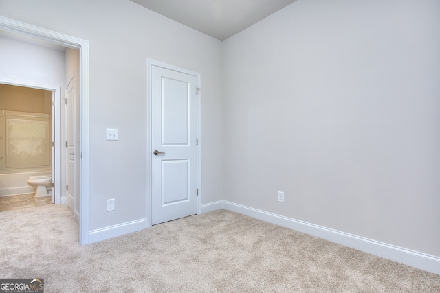 unfurnished bedroom with ensuite bath and light colored carpet