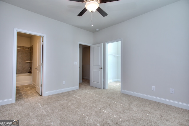 unfurnished bedroom with a closet, ceiling fan, ensuite bathroom, a walk in closet, and light colored carpet