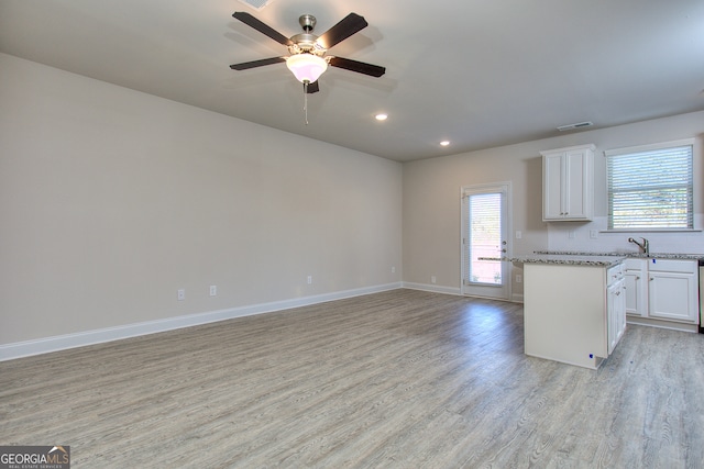 kitchen with light hardwood / wood-style floors, white cabinets, a kitchen island, light stone countertops, and ceiling fan