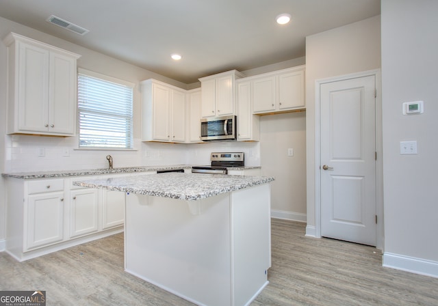 kitchen with light wood-type flooring, a center island, tasteful backsplash, white cabinets, and stainless steel appliances