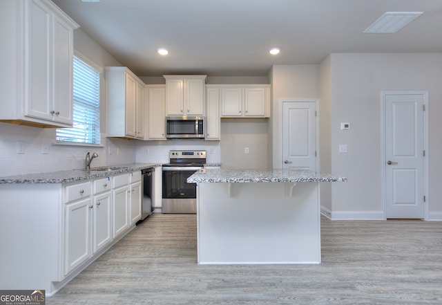 kitchen with a kitchen island, white cabinetry, light hardwood / wood-style flooring, and stainless steel appliances