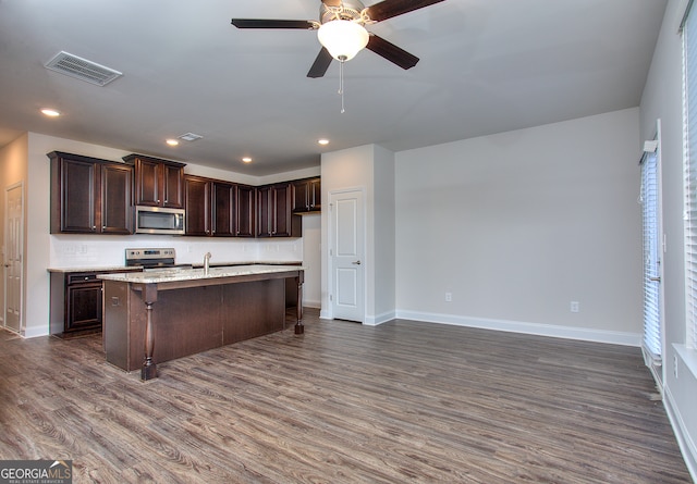 kitchen featuring dark brown cabinets, dark wood-type flooring, stainless steel appliances, a center island with sink, and ceiling fan