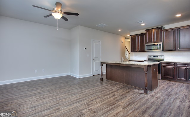 kitchen with ceiling fan, a kitchen island with sink, appliances with stainless steel finishes, dark hardwood / wood-style floors, and a breakfast bar area