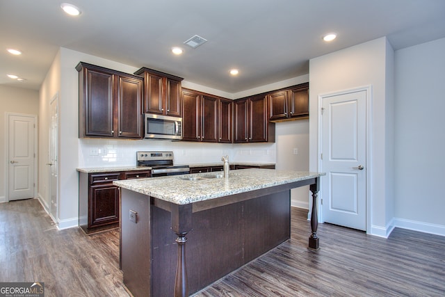 kitchen featuring light stone counters, dark wood-type flooring, sink, stainless steel appliances, and a center island with sink