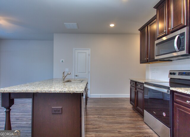 kitchen with appliances with stainless steel finishes, decorative backsplash, an island with sink, dark hardwood / wood-style flooring, and sink