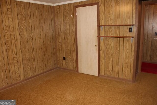 carpeted empty room featuring wood walls and ornamental molding