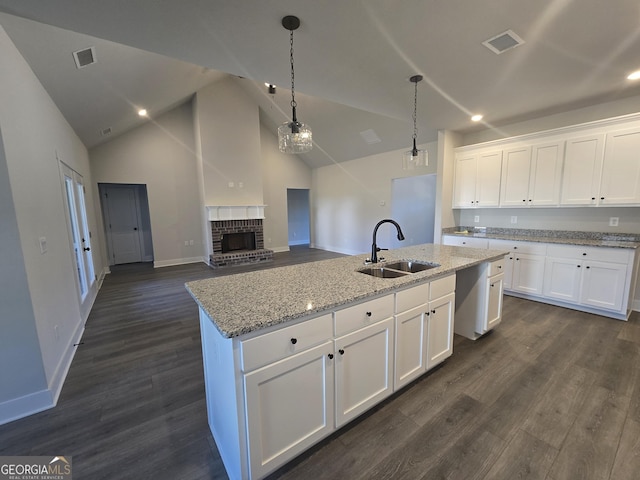 kitchen with sink, light stone countertops, an island with sink, and white cabinets