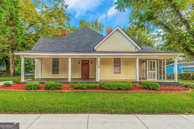 country-style home featuring covered porch, roof with shingles, a chimney, and a front yard