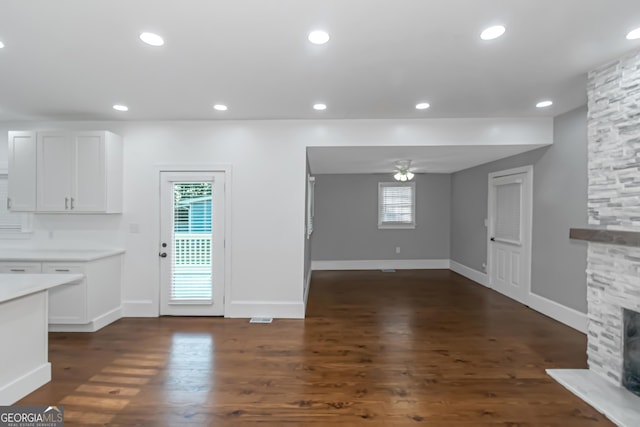 unfurnished living room featuring recessed lighting, dark wood-type flooring, a ceiling fan, a stone fireplace, and baseboards