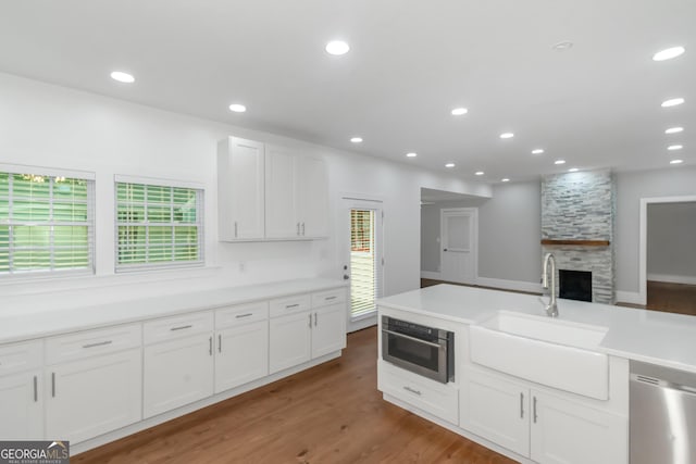 kitchen with wood finished floors, stainless steel appliances, a stone fireplace, white cabinetry, and a sink