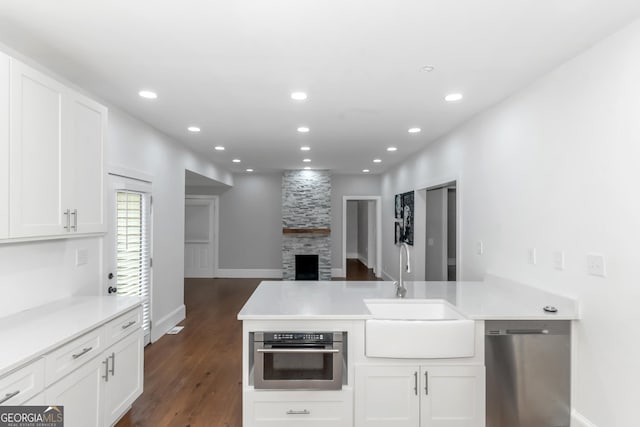 kitchen with stainless steel appliances, a peninsula, dark wood-style flooring, a sink, and white cabinetry