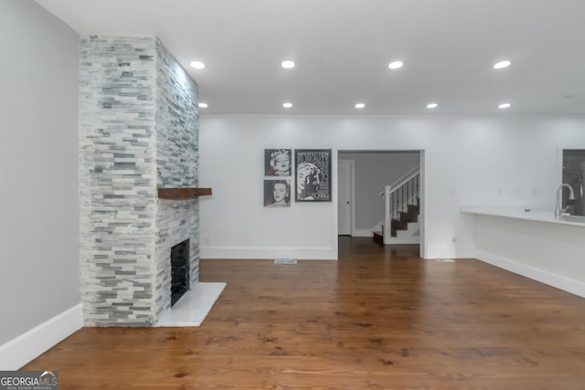 unfurnished living room featuring recessed lighting, a fireplace, a sink, wood finished floors, and stairs