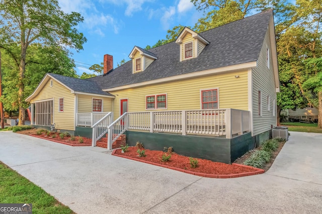 new england style home with a shingled roof, a chimney, and central AC unit