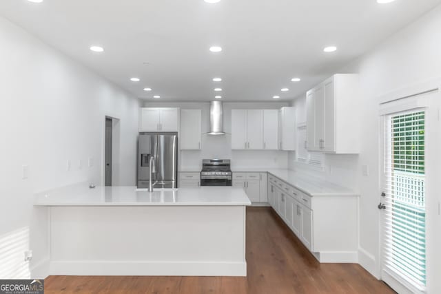 kitchen featuring stainless steel appliances, wall chimney exhaust hood, a peninsula, and white cabinets