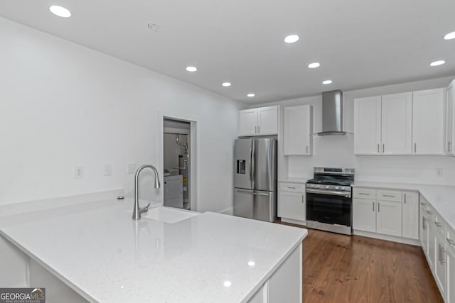 kitchen featuring dark wood finished floors, stainless steel appliances, a sink, wall chimney range hood, and a peninsula