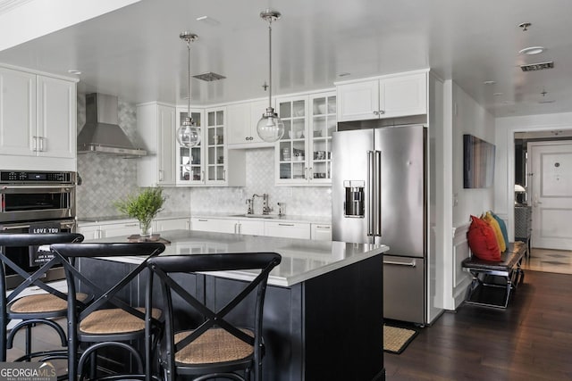 kitchen with a kitchen island, glass insert cabinets, stainless steel appliances, light countertops, and wall chimney range hood