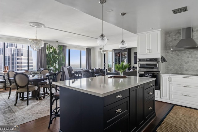 kitchen featuring decorative light fixtures, light countertops, double oven, white cabinets, and wall chimney exhaust hood