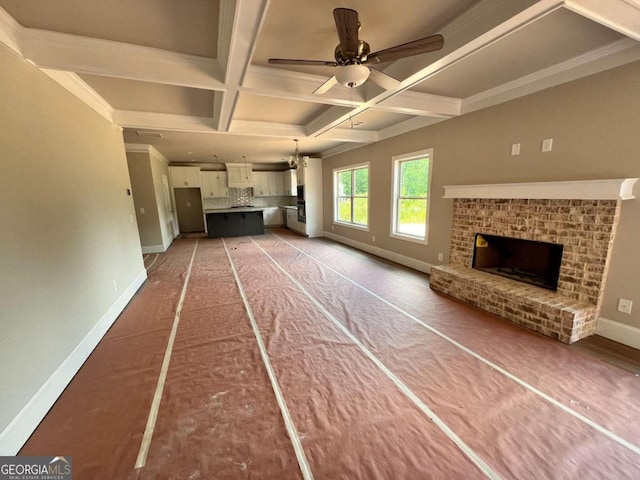 unfurnished living room featuring a brick fireplace, beam ceiling, ceiling fan, ornamental molding, and coffered ceiling