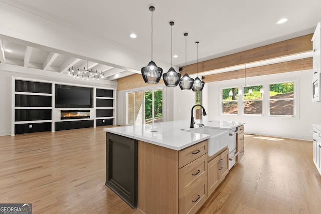 kitchen featuring a kitchen island with sink, decorative light fixtures, sink, beam ceiling, and light brown cabinets