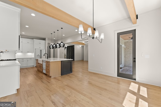 kitchen with a large island with sink, white cabinetry, light hardwood / wood-style flooring, decorative light fixtures, and beam ceiling