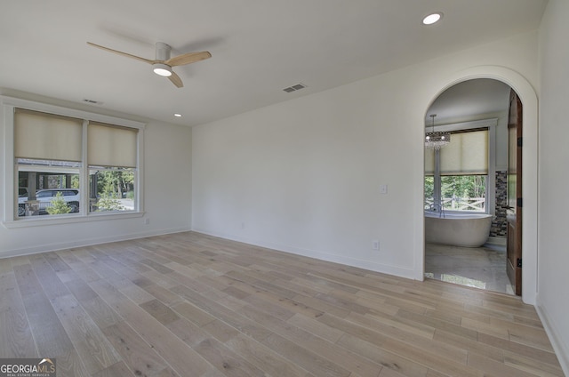 unfurnished room with ceiling fan with notable chandelier and light hardwood / wood-style floors