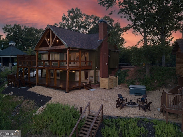 back house at dusk featuring an outdoor fire pit, a hot tub, and a deck