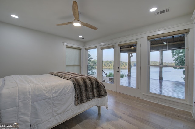 bedroom with a water view, access to exterior, multiple windows, and light wood-type flooring