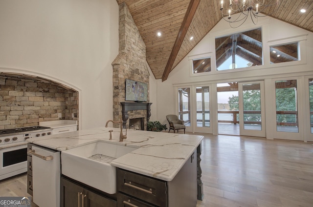 kitchen featuring light stone counters, a fireplace, gas stove, a center island with sink, and wooden ceiling