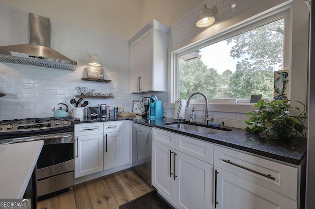 kitchen with appliances with stainless steel finishes, dark hardwood / wood-style floors, sink, white cabinets, and wall chimney exhaust hood