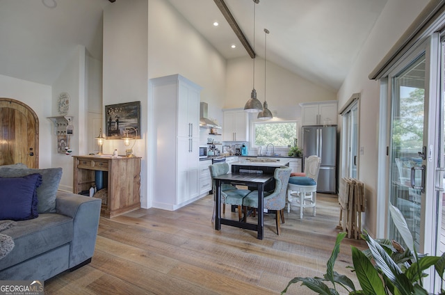 kitchen featuring wall chimney exhaust hood, hanging light fixtures, light wood-type flooring, stainless steel fridge, and white cabinets