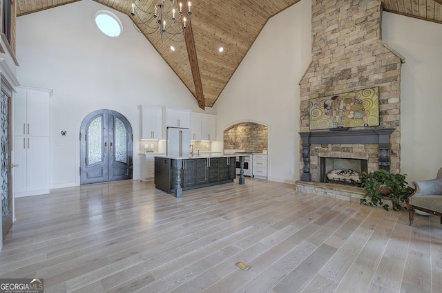 unfurnished living room featuring a stone fireplace, high vaulted ceiling, light hardwood / wood-style floors, wood ceiling, and french doors