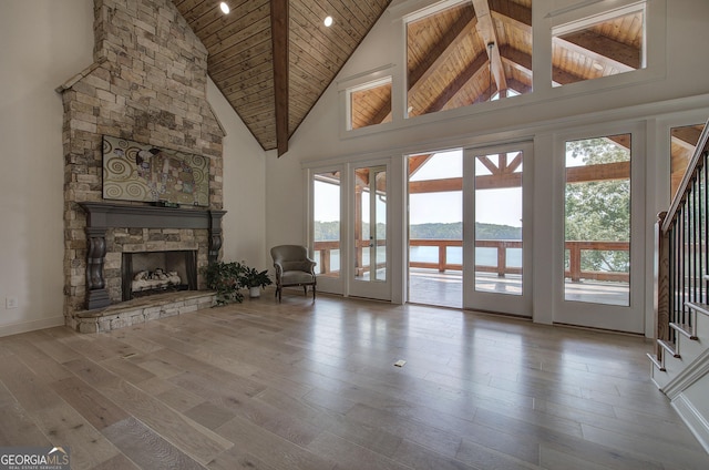 unfurnished living room with a water view, high vaulted ceiling, wooden ceiling, light wood-type flooring, and a fireplace